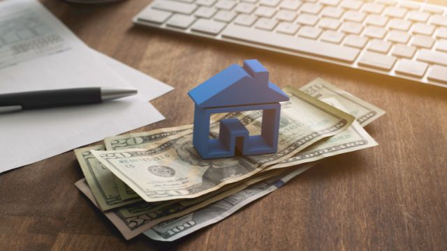 a blue home figurine resting on money with a contract in the background